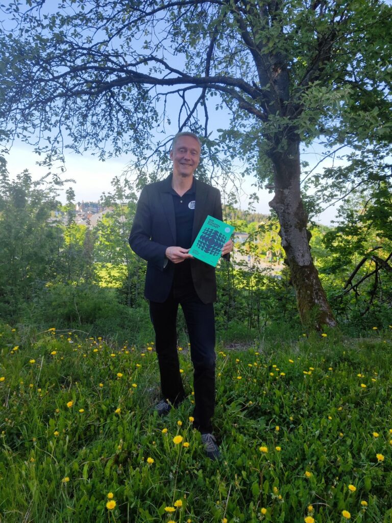 Holger Holland mit dem Buch „Wir schaffen Zukunft“ unter einem Baum