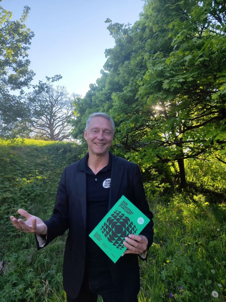 Holger Holland mit dem Buch „Wir schaffen Zukunft“ auf einer Wiese